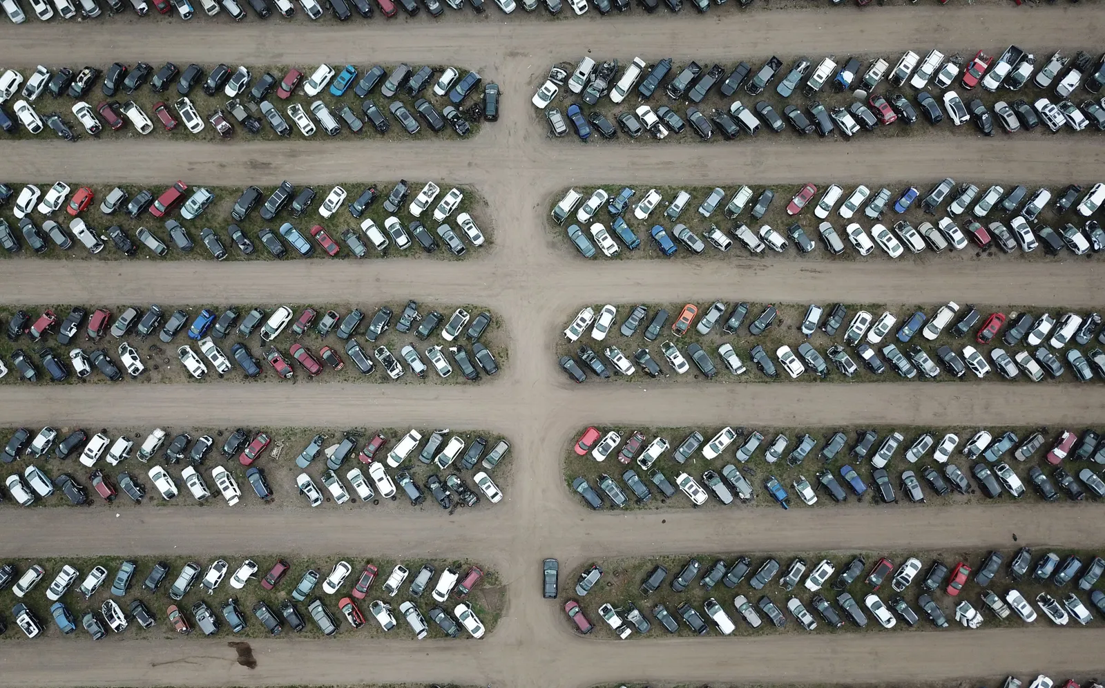 Aerial view of hundreds of used cars parked in long rows across a dirt storage lot