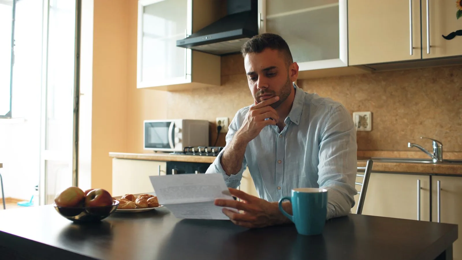 Man sitting at a kitchen table reading a letter in morning light