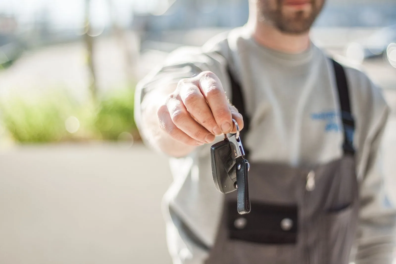 Person holding out a car key and fob toward the camera on a sunlit street