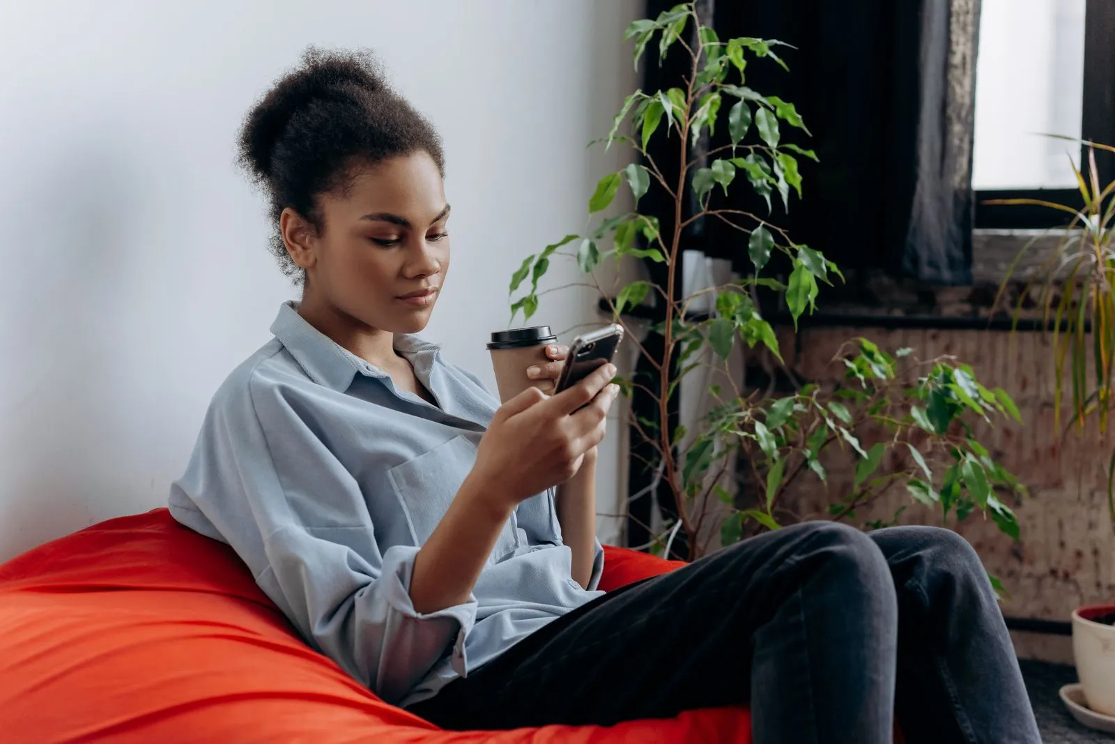 Person sitting at home checking a phone while holding a coffee cup