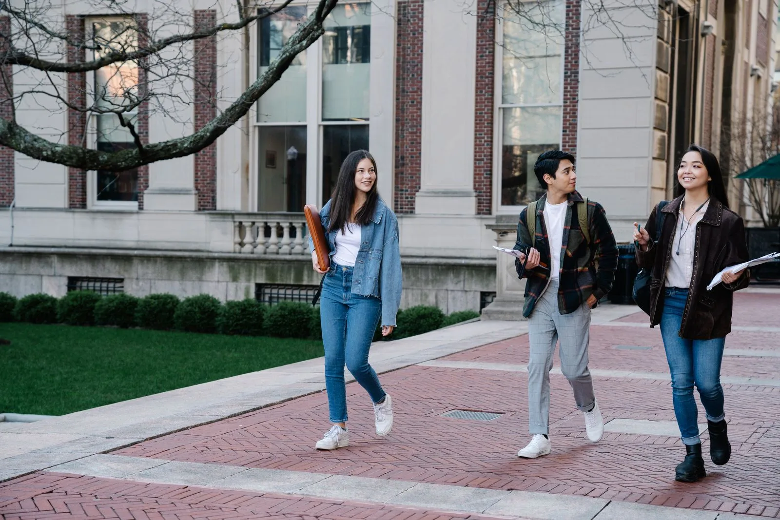 Three college students walking across a brick campus walkway past a university building