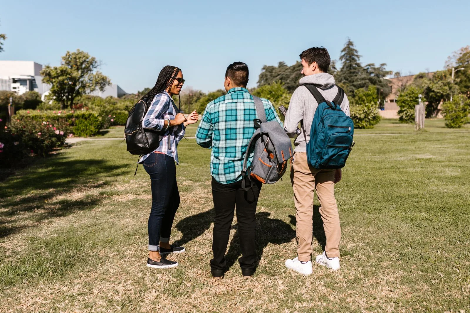 Three students with backpacks talking on a sunny college campus lawn