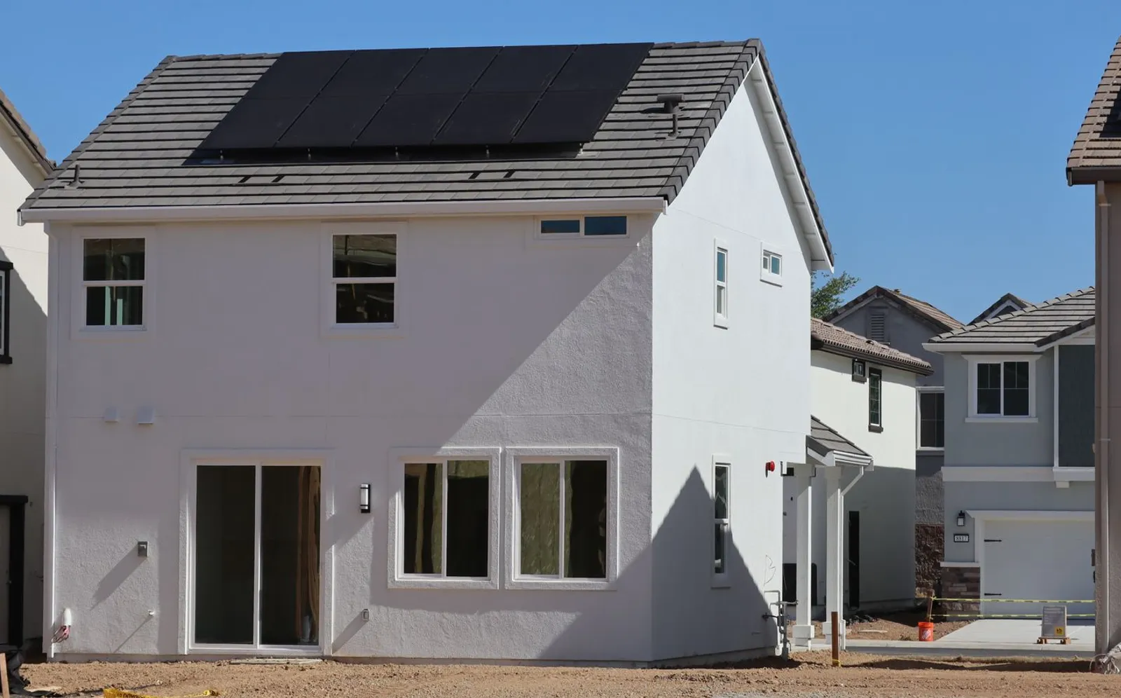 A newly built two-story home with black solar panels on the roof under a clear sky