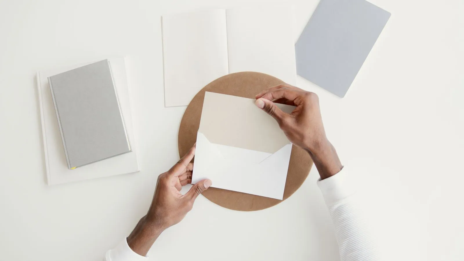 Overhead view of a person opening a plain envelope on a clean desk