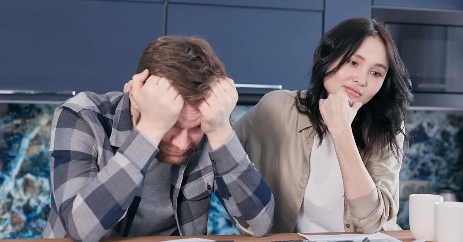 A couple sitting at a kitchen table looking worried while going through paperwork