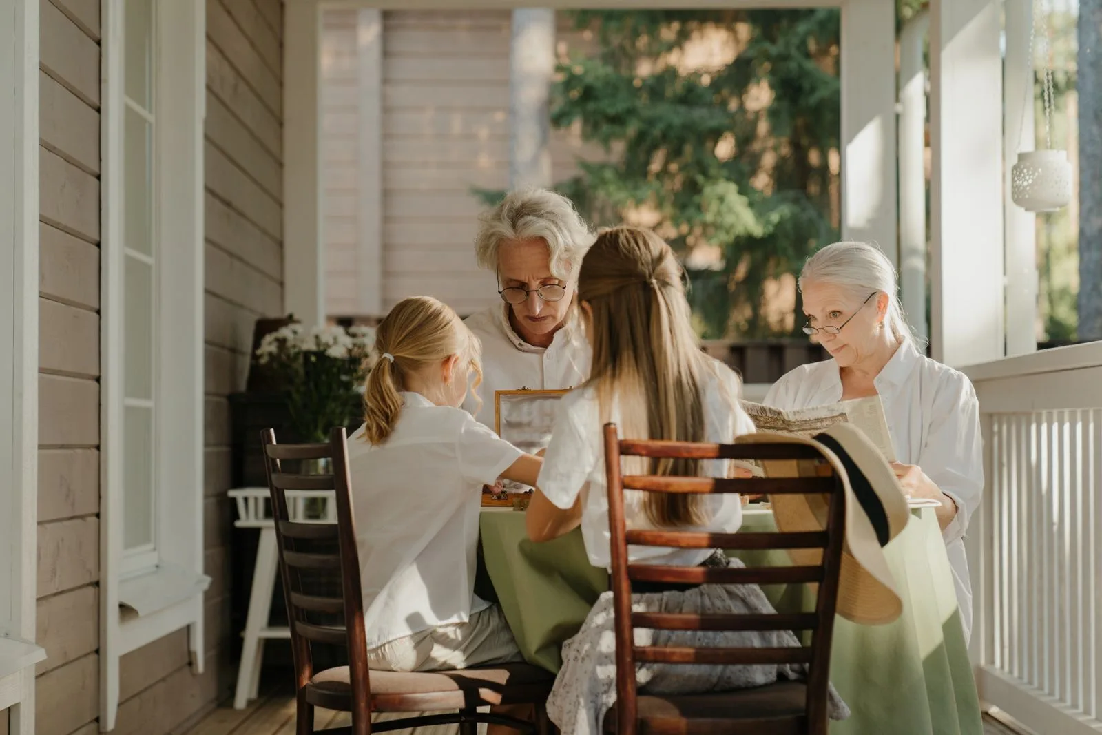 Two grandmothers and two granddaughters sitting together at a table on a sunlit porch