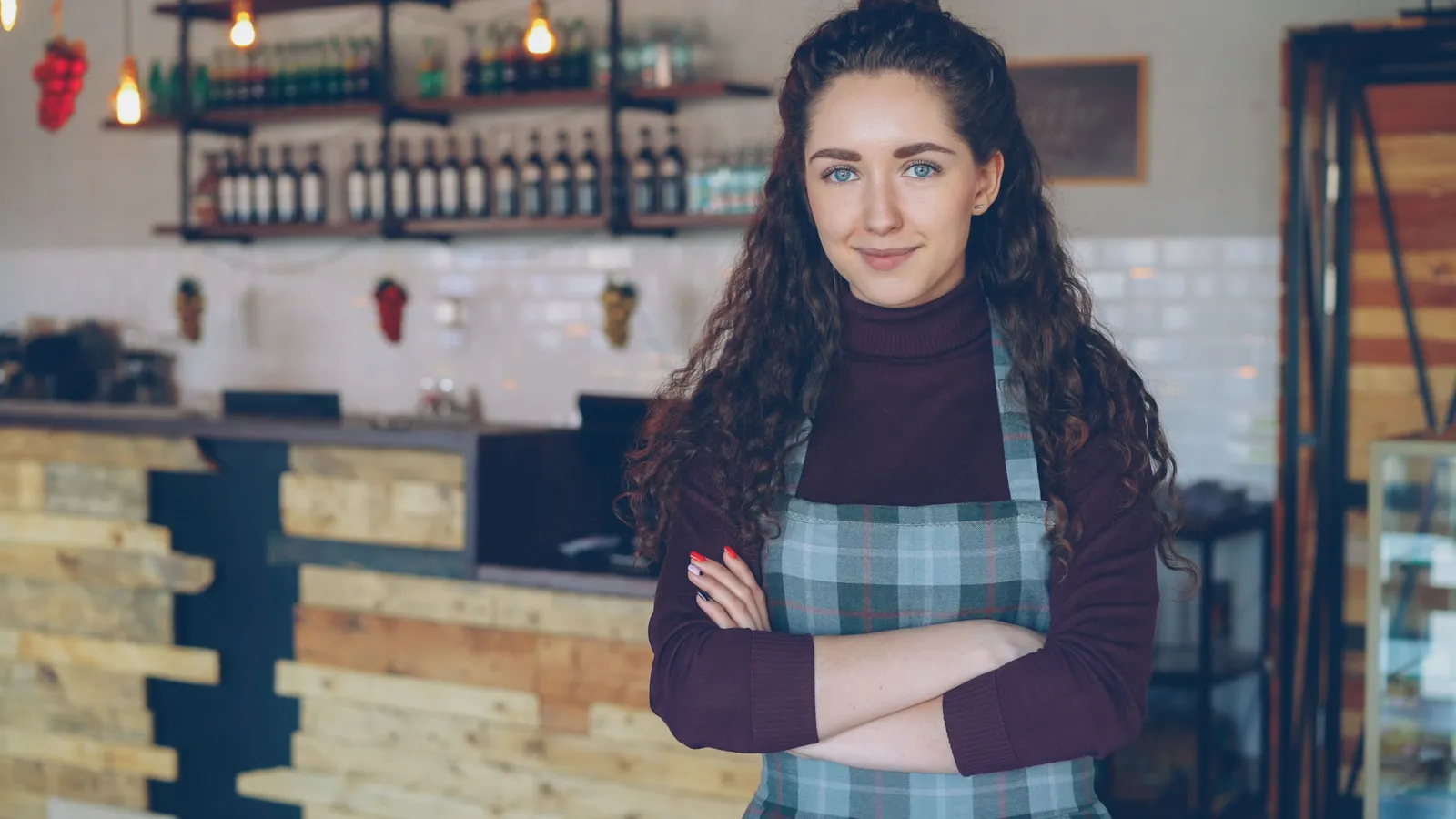 A cafe owner standing with arms crossed behind the counter of a small rustic coffee shop
