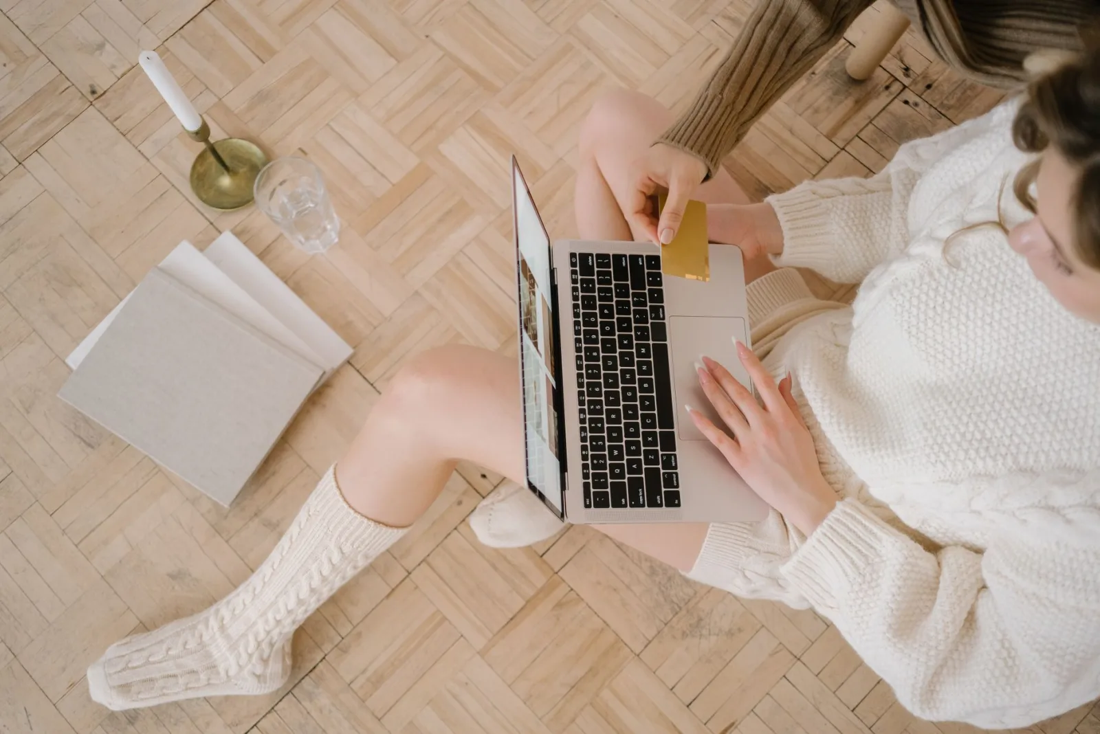 Overhead view of a woman sitting on the floor shopping online with a laptop and a credit card