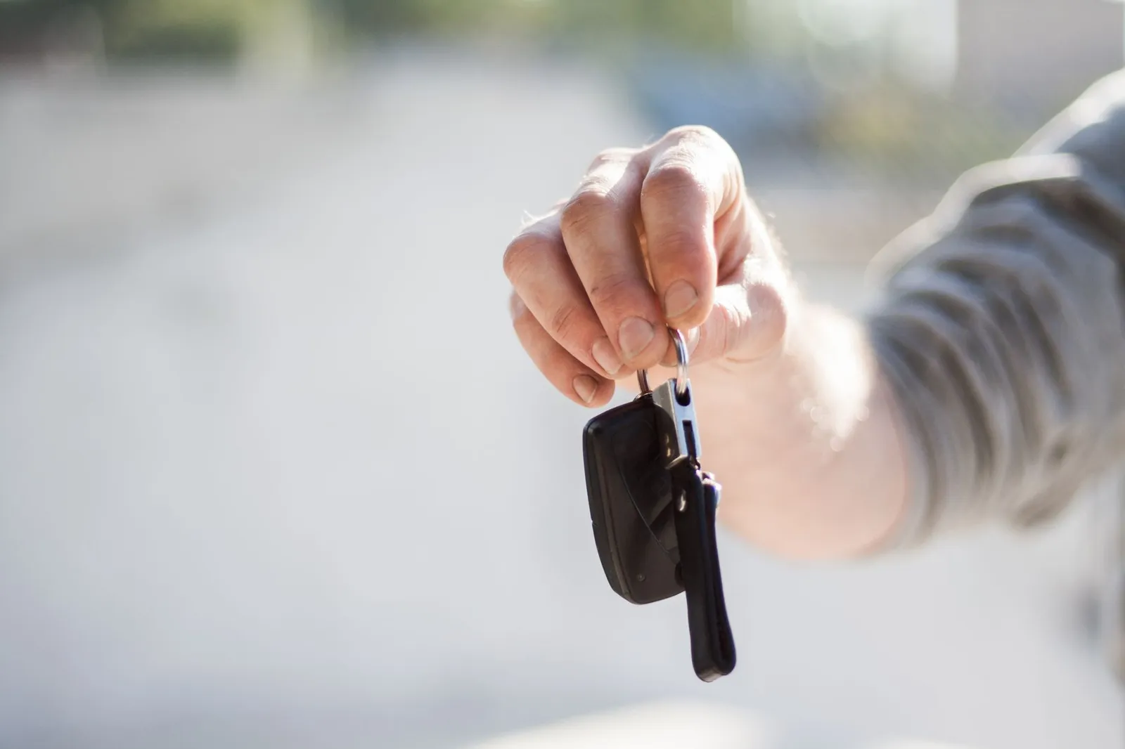 A hand holding out a car key on a keyring in bright daylight