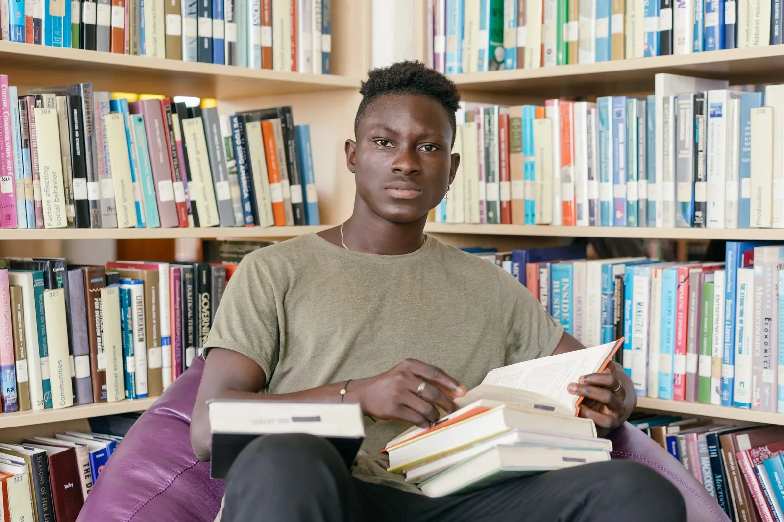 A student sitting in a university library with a stack of open books