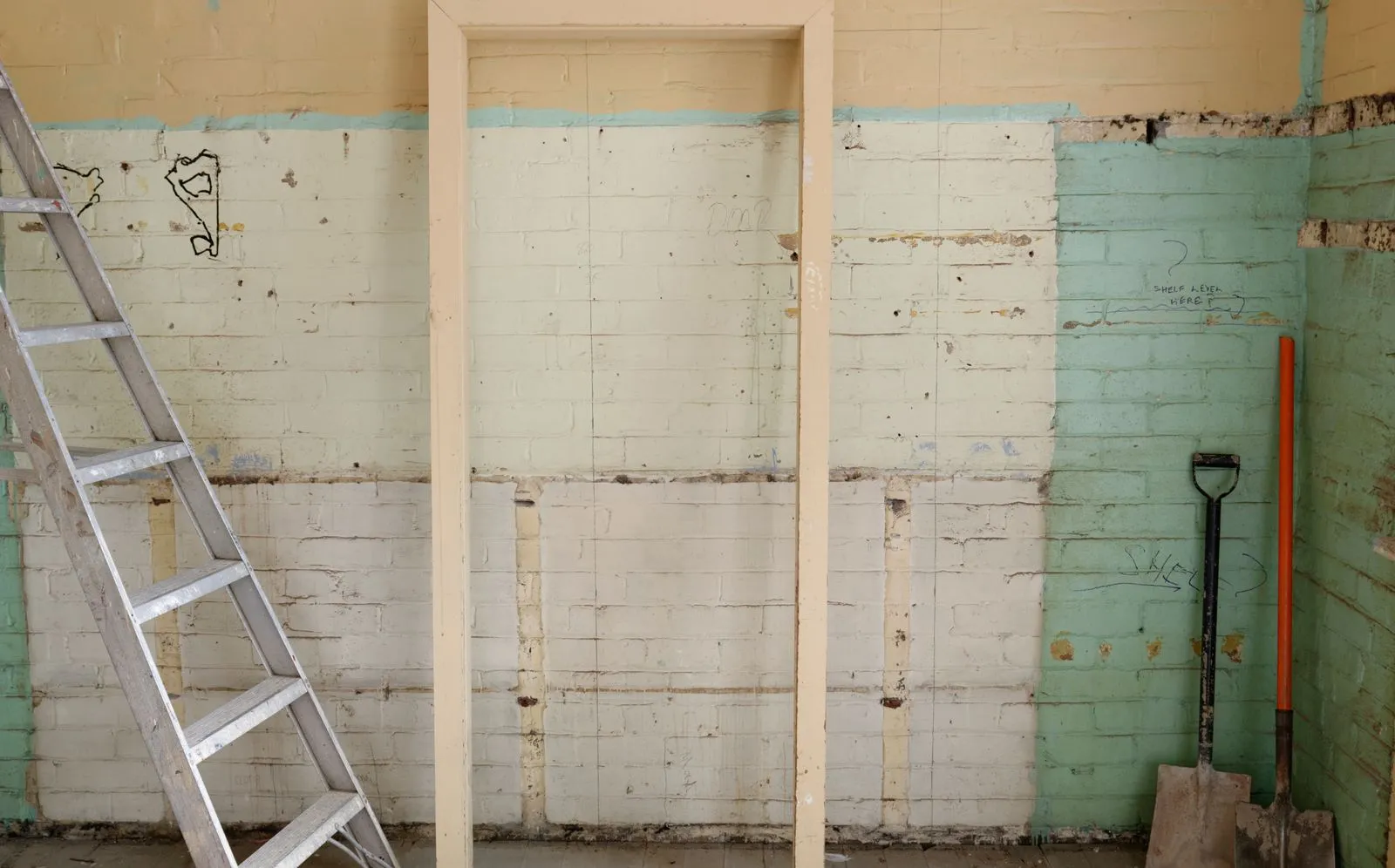 A half finished room repair with a ladder and shovel against a stripped brick wall