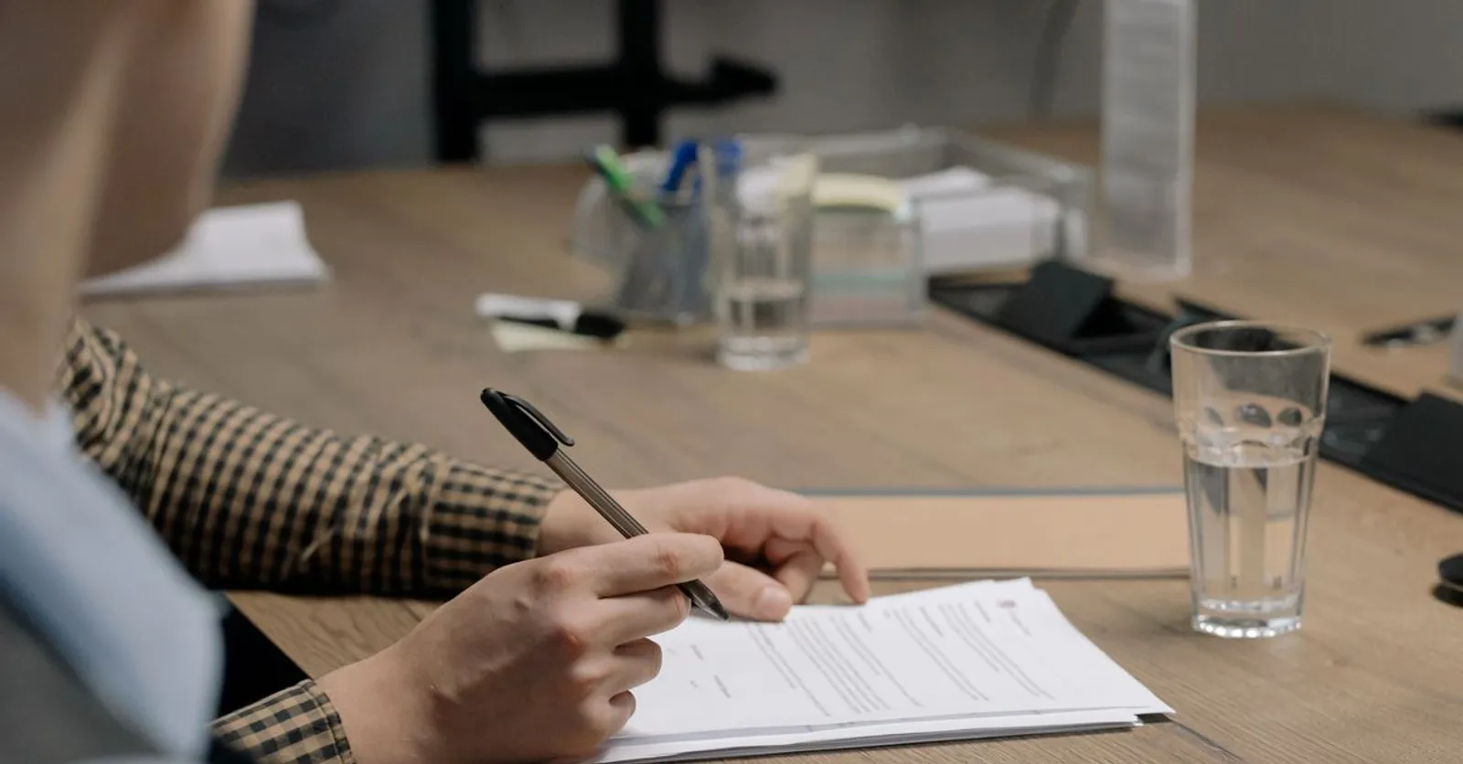 A person holding a pen over a printed contract on an office desk