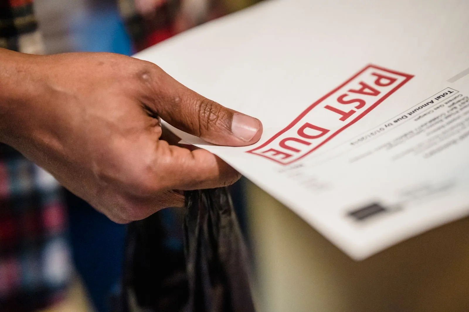 A hand holding a bill stamped PAST DUE in red ink