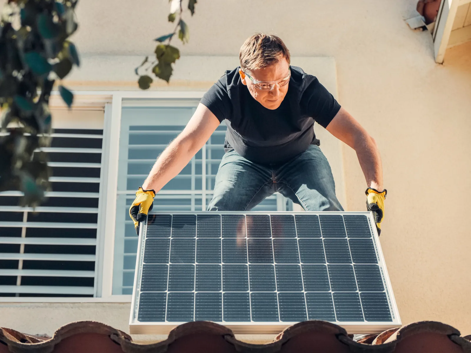 A worker in safety glasses installing a solar panel on a house roof