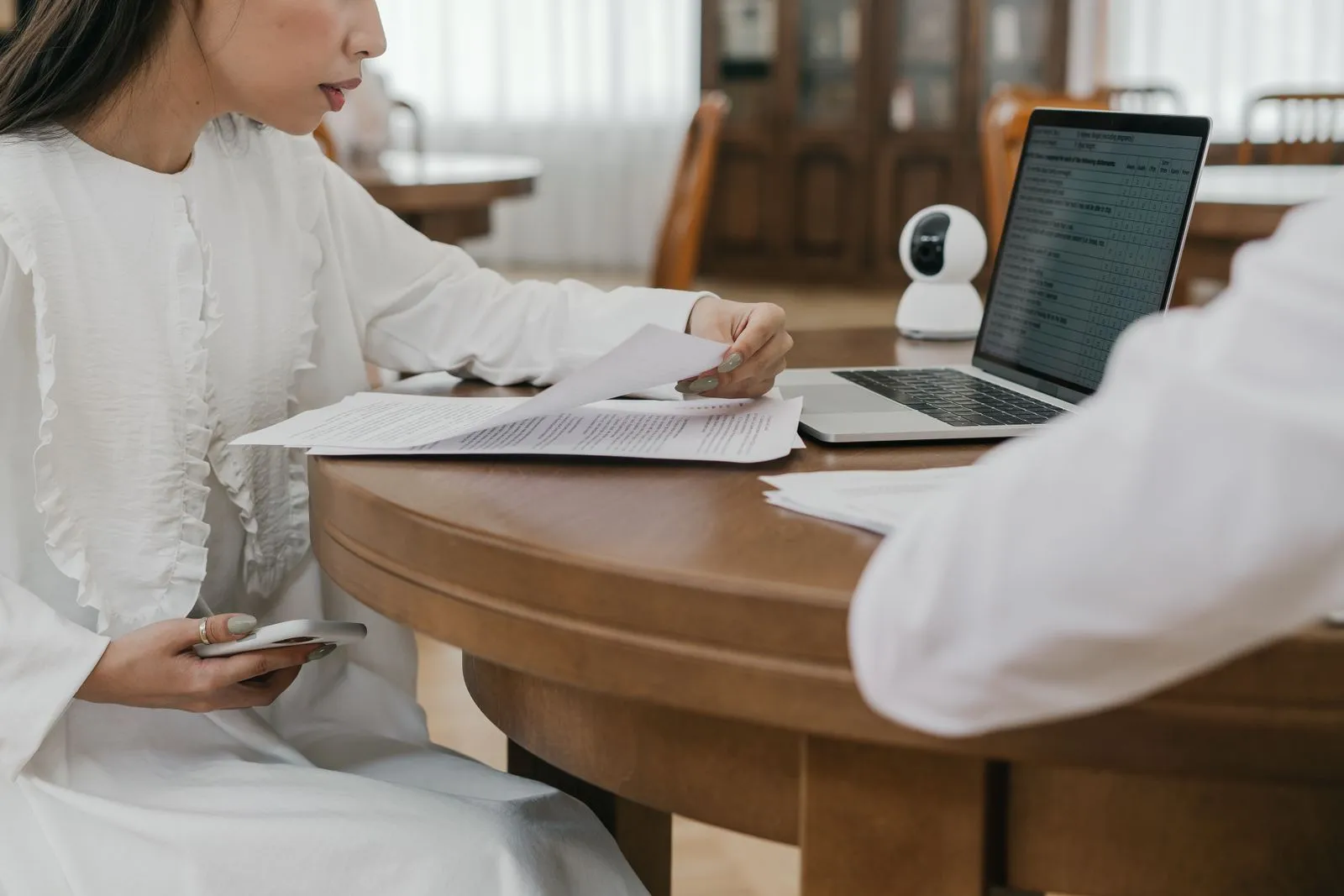 Person reviewing printed documents at a wooden table beside an open laptop