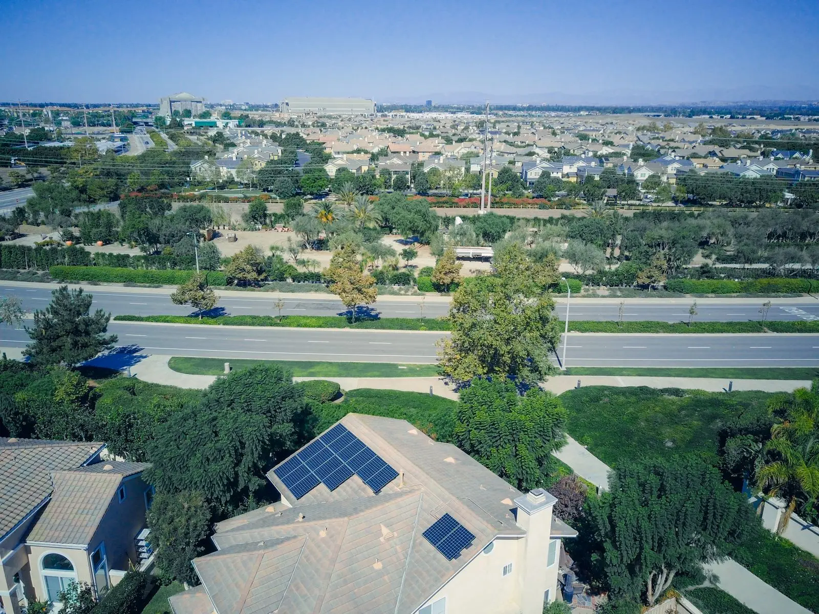 Aerial view of a suburban home with rooftop solar panels beside a wide boulevard