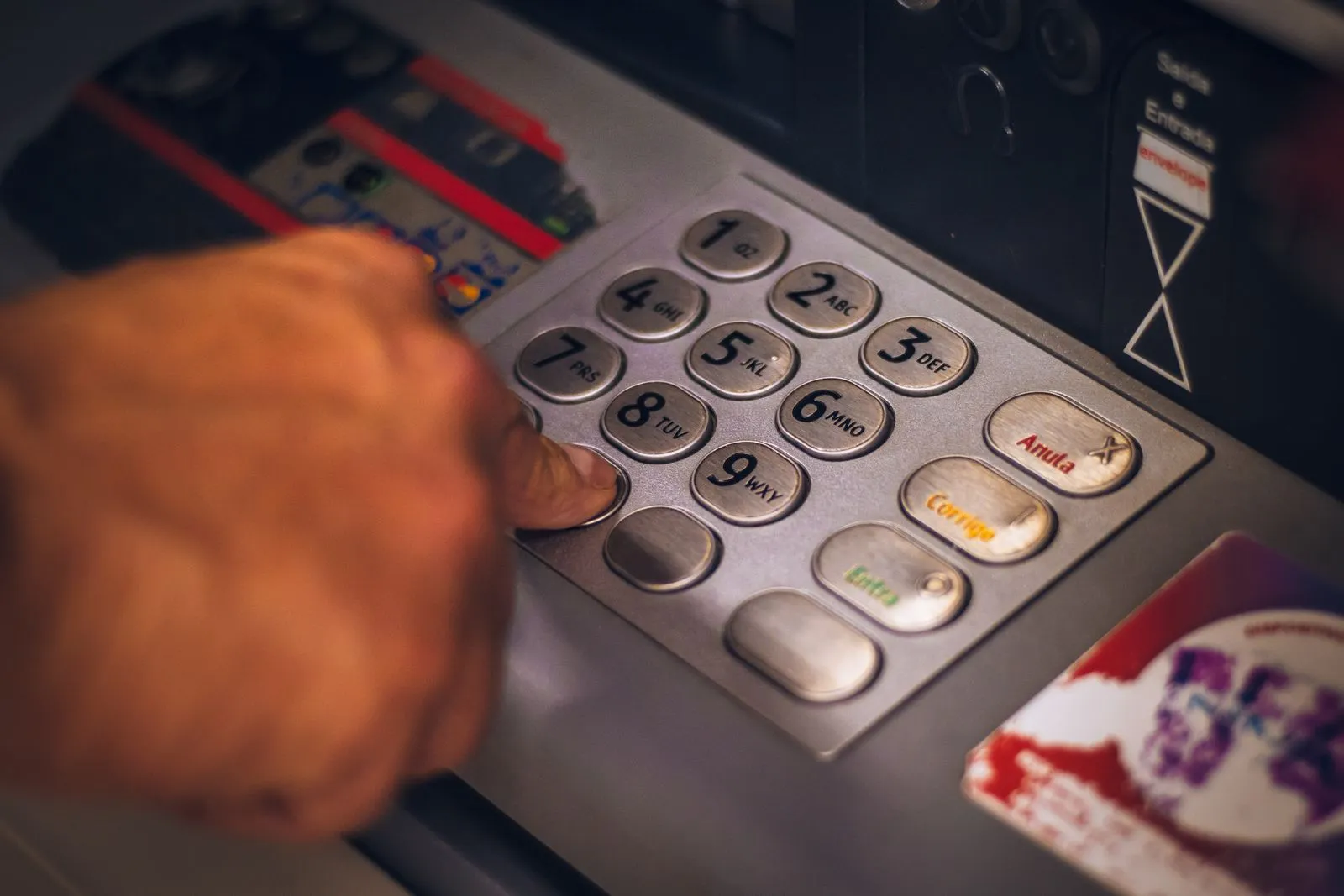 Close-up of a hand pressing a key on a worn metal ATM keypad