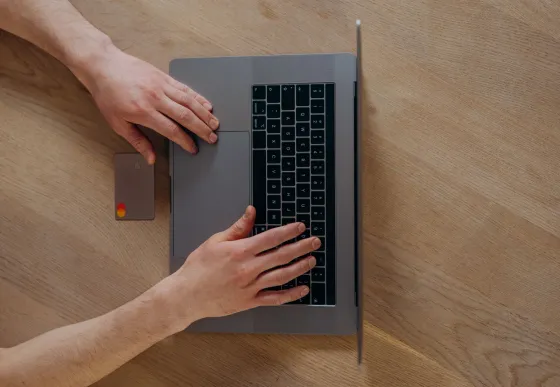 A person using a laptop beside a credit card on a wooden table