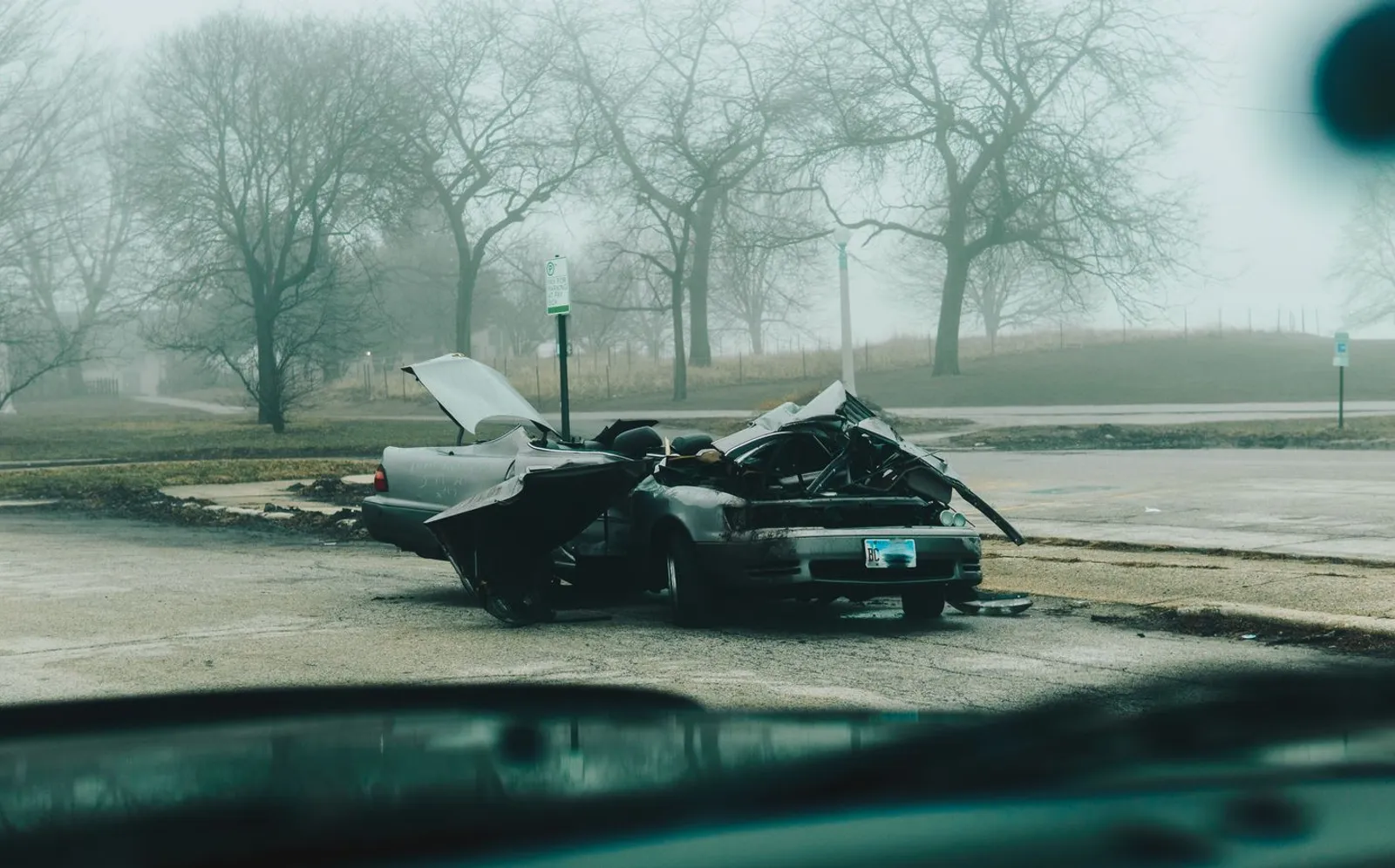 Severely damaged car sitting on an empty street on a foggy morning