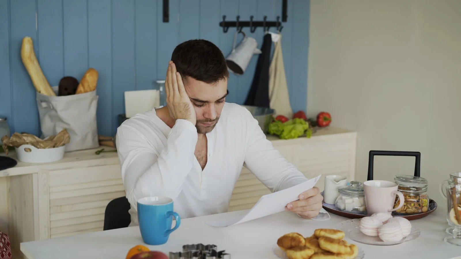 Man in a white shirt reading a document at a kitchen table over breakfast