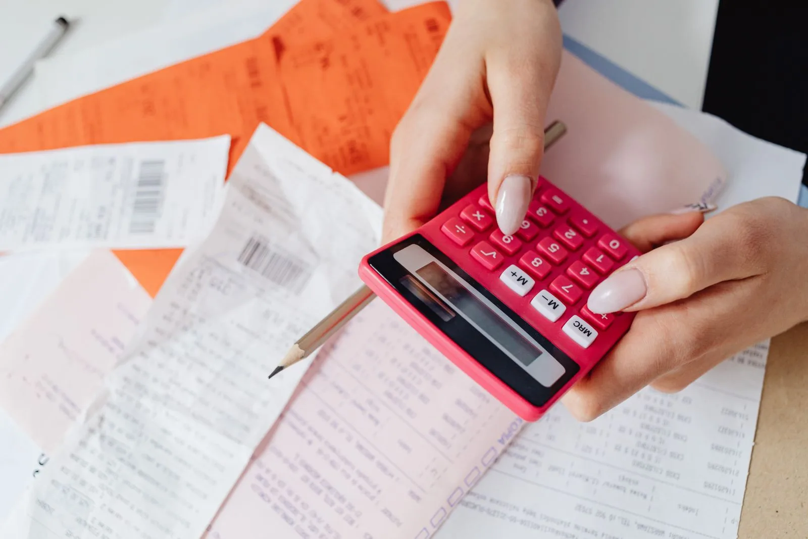 Hands working a calculator over a spread of paper receipts and statements
