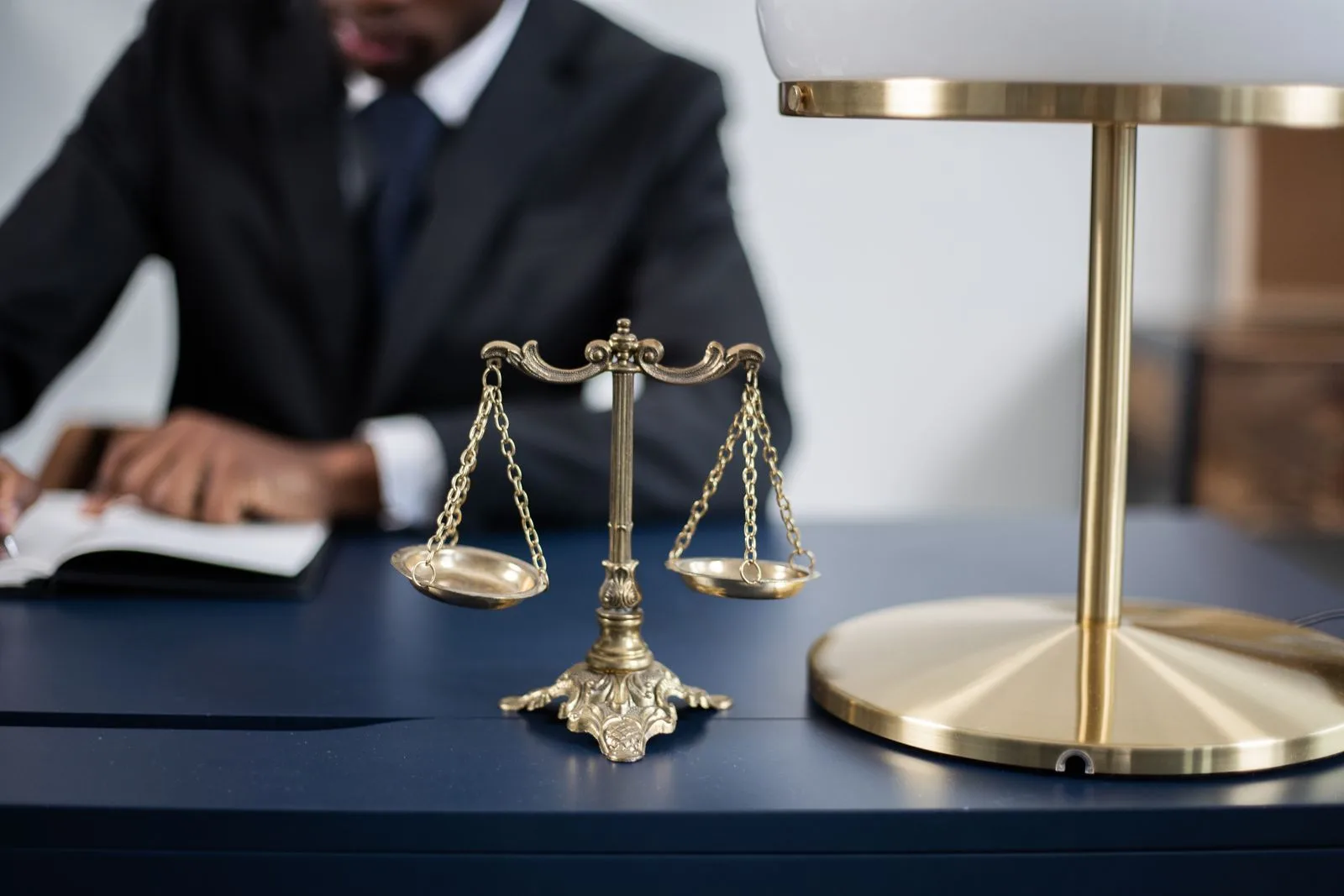 Brass scales of justice on a dark desk with a lawyer working behind them