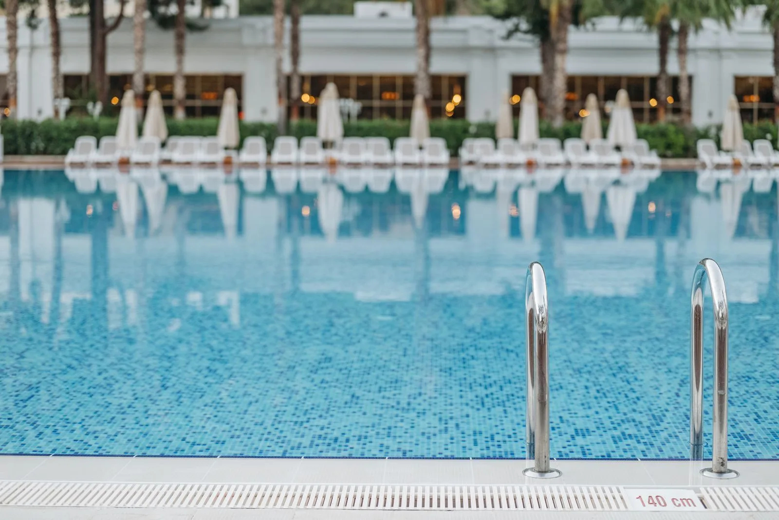 An empty resort pool with rows of unused loungers and closed parasols