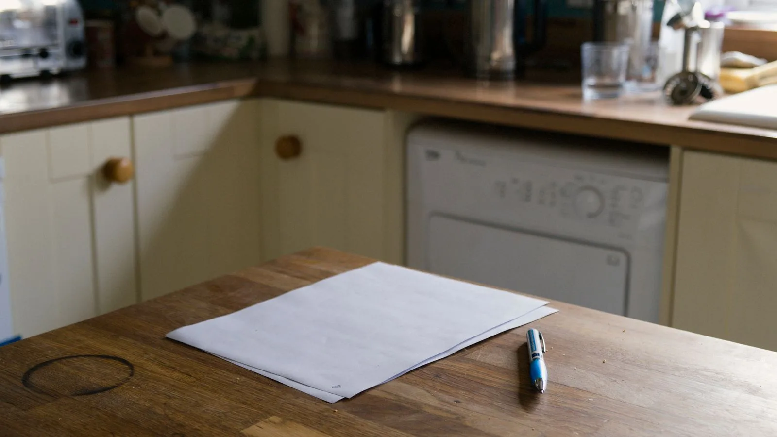 A blank sheet of paper and a pen left on a kitchen table in a quiet house