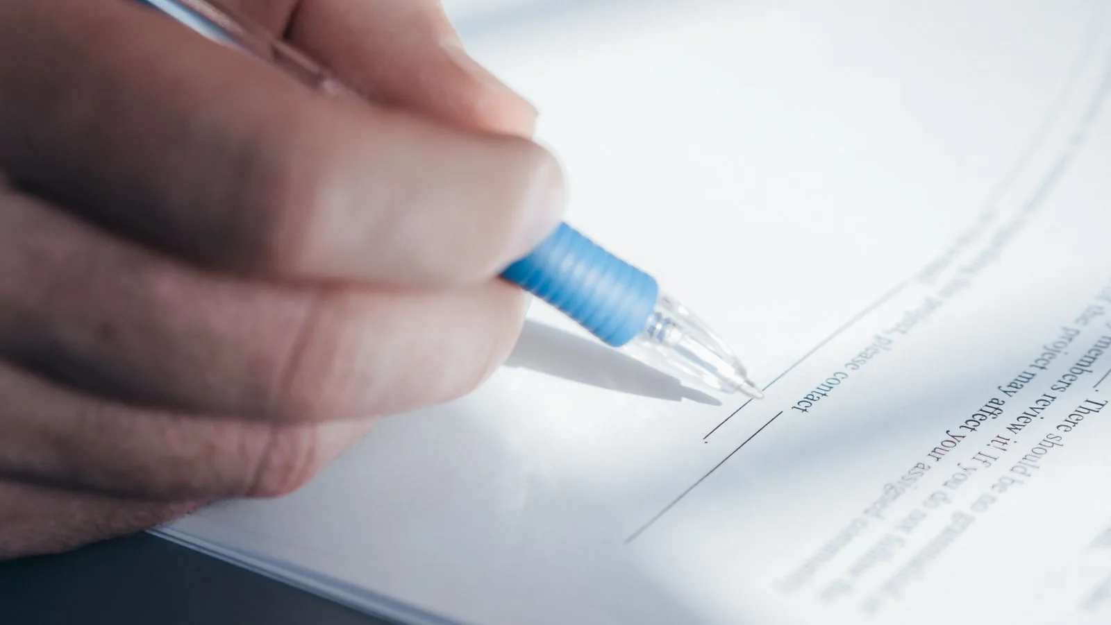 A hand lowering a pen toward the signature line of a printed contract