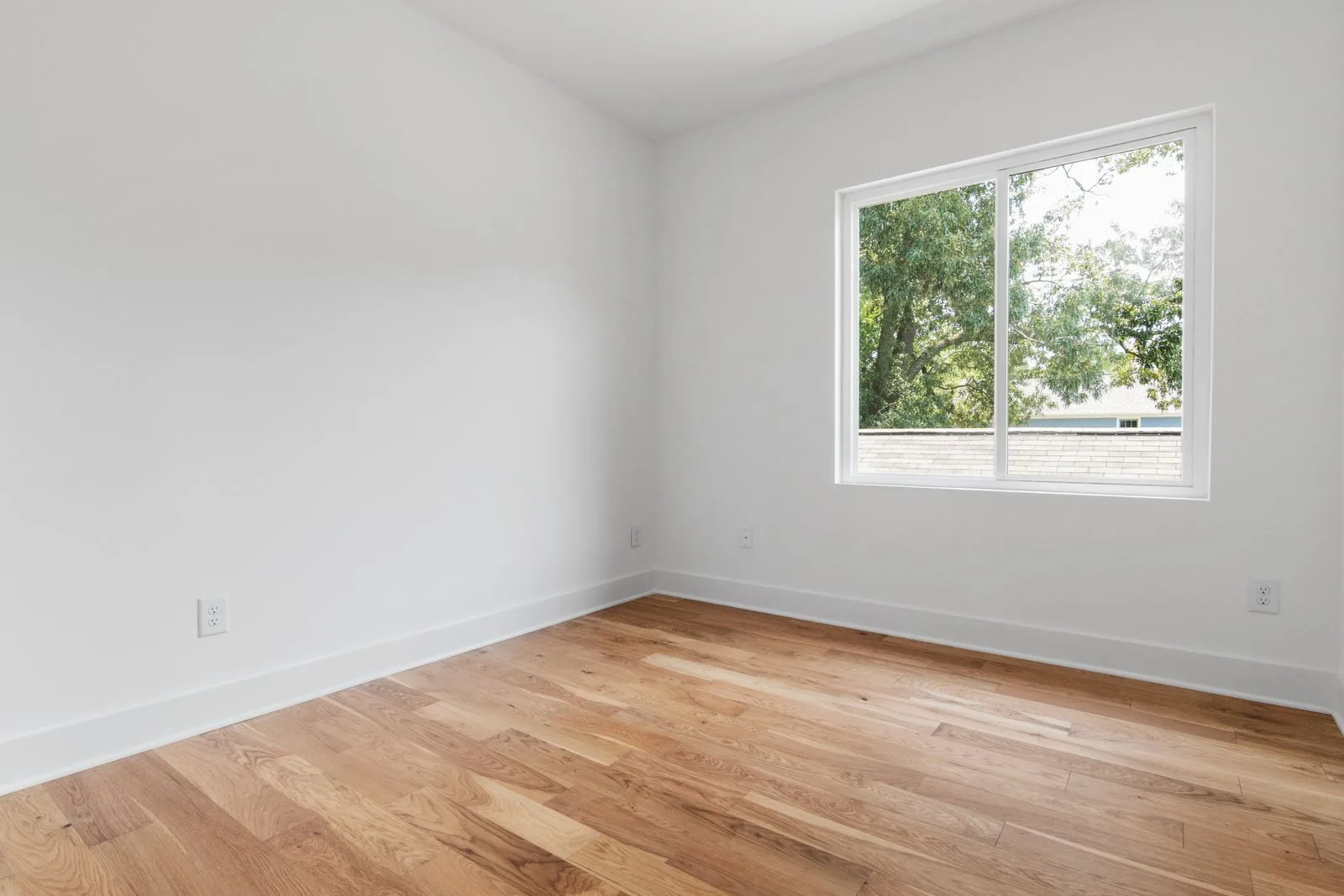 An empty room with bare walls, wooden floors and a window looking onto trees